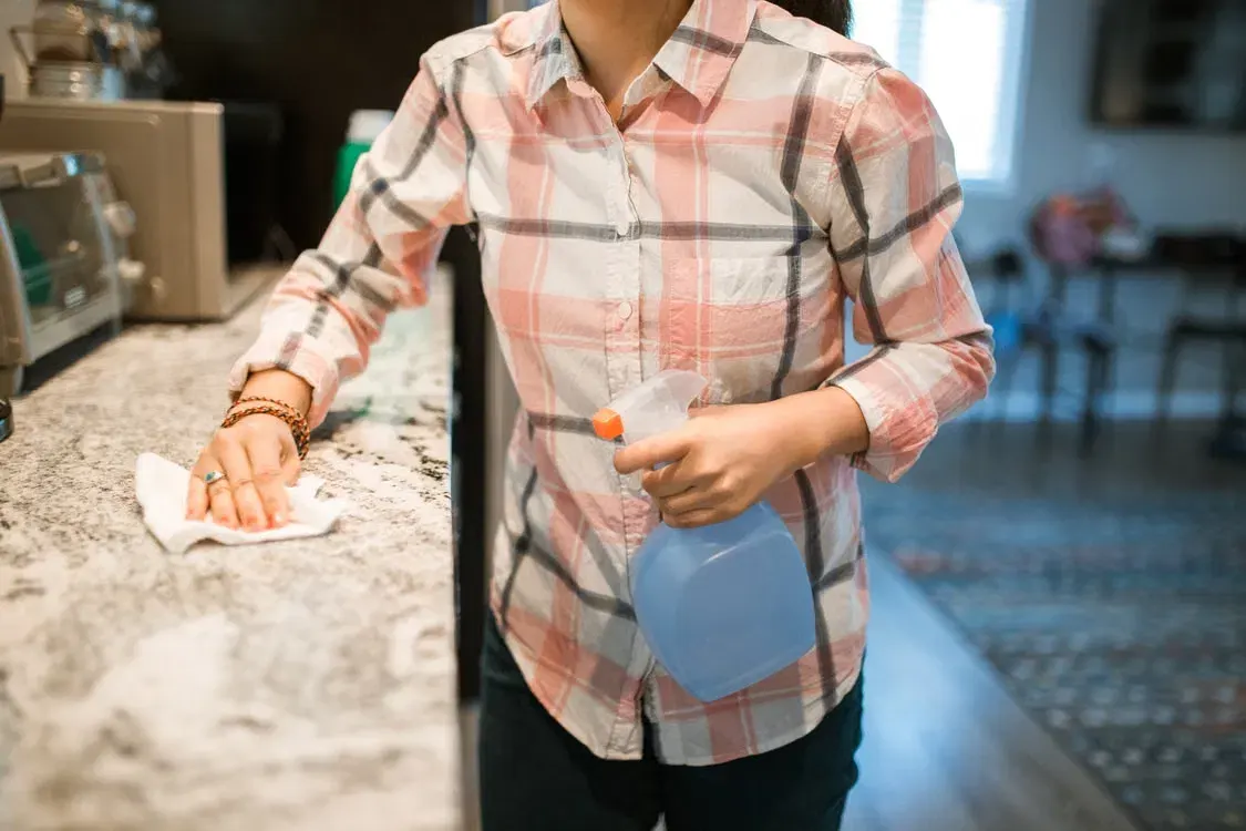 Cleaner wiping down a granite kitchen bench with an eco-friendly spray bottle
